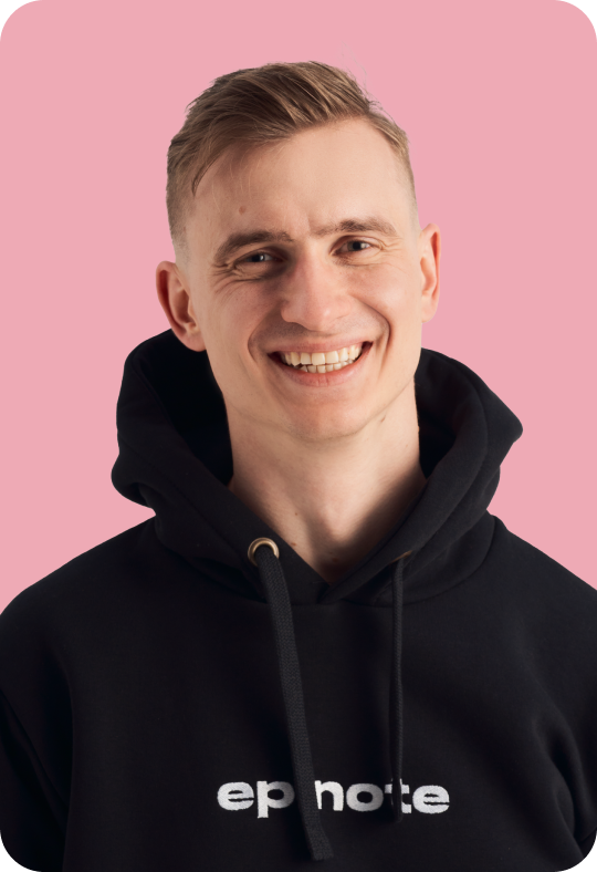 A person with short blond hair, smiling and wearing a black hoodie with the text 